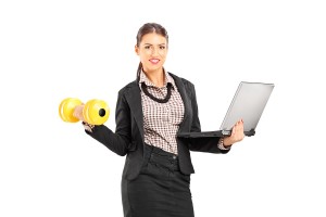 Busy smiling businesswoman holding a laptop and lifting a dumbbe