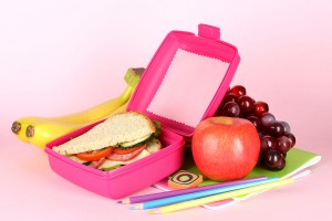 Lunch box with sandwich,fruit and stationery on pink background